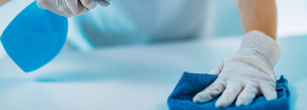 Close-up of gloved hands cleaning surface with spray bottle and cloth.