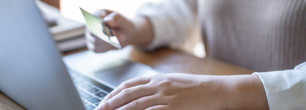 Close-up of hands typing on laptop keyboard while holding credit card.