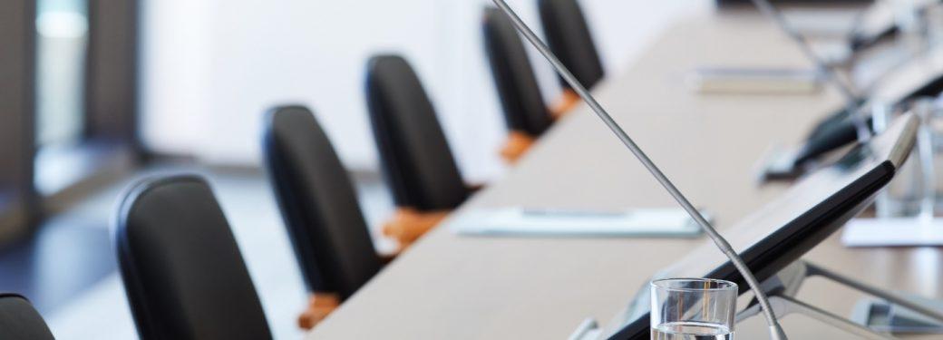 Empty conference room with microphones on table and chairs arranged around.