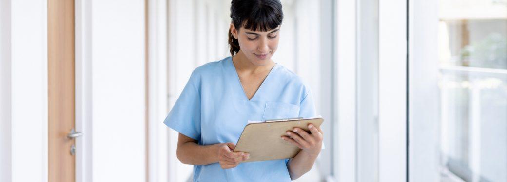 Registered Massage Therapist in blue scrubs reading from clipboard while walking down hallway.