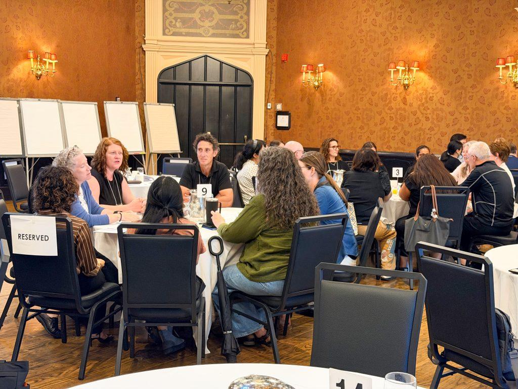 Massage Therapy educators sitting in round tables engaged in group discussions with each other.